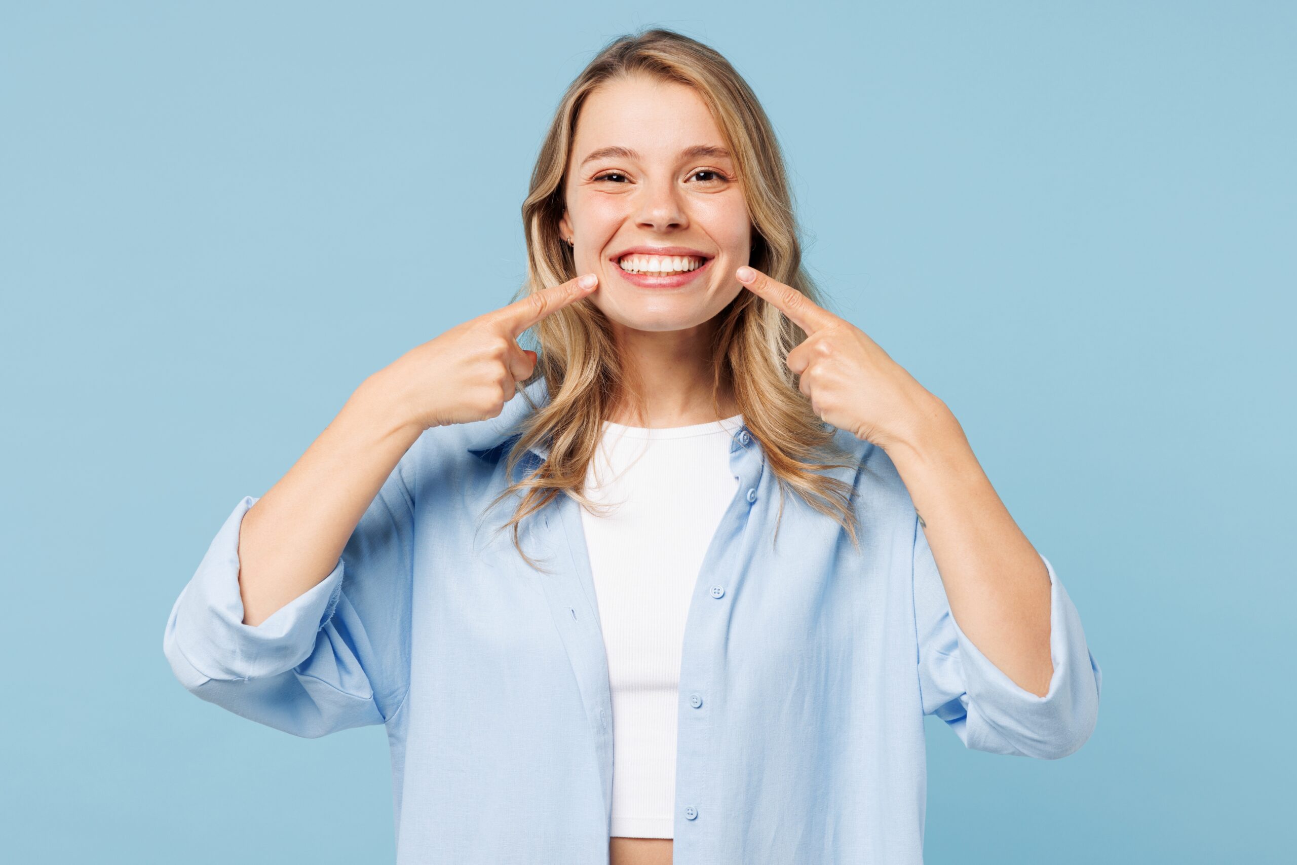 young woman pointing to her perfect smile against a light blue background