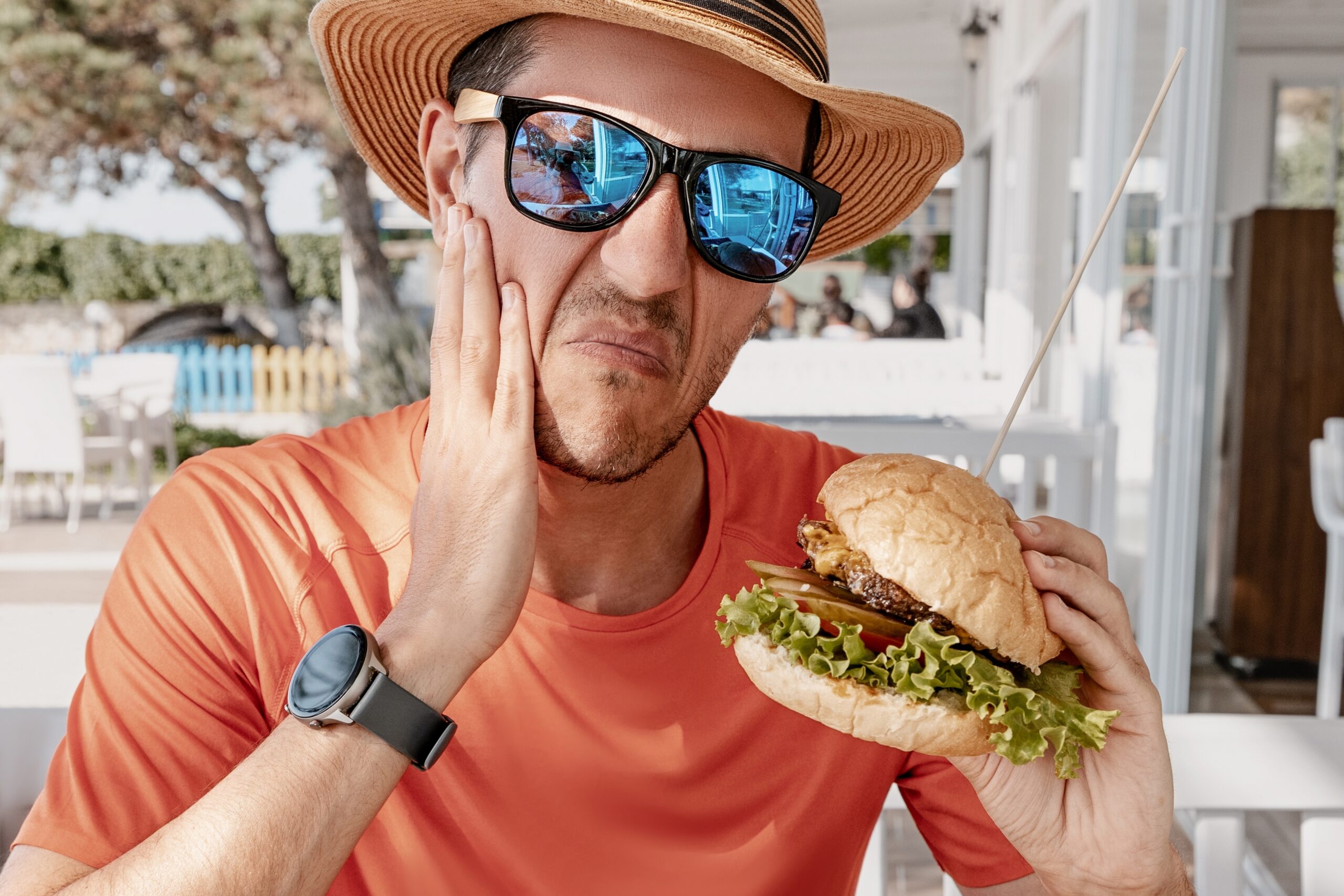 man eating a burger suffering from tooth pain