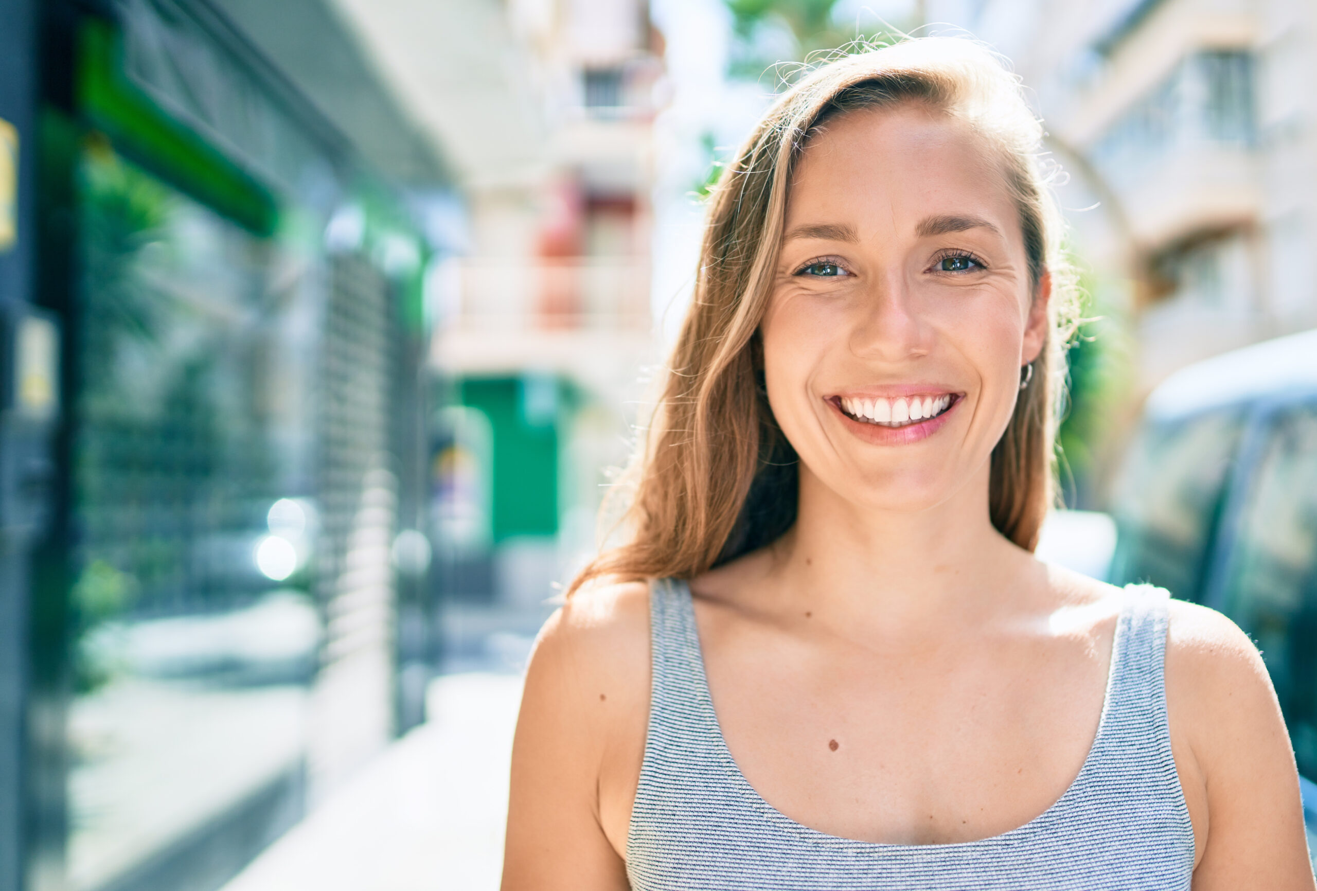 young blonde woman smiling on a city street, perfect white smile